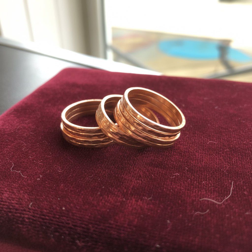 A stack of textured copper bands displayed on a black ring stand, set against a dark gray textured surface.